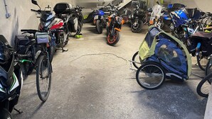 Un garaje para estacionamiento con varias motocicletas y bicicletas, piso de concreto y una escalera al fondo.