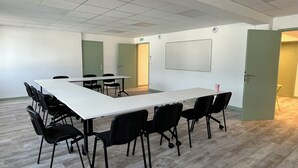 Un salón de conferencias con una larga mesa, sillas negras, una pizarra y una puerta.