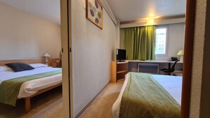 Habitación de hotel con dos camas, un escritorio con computadora, televisor y ventana con cortinas.