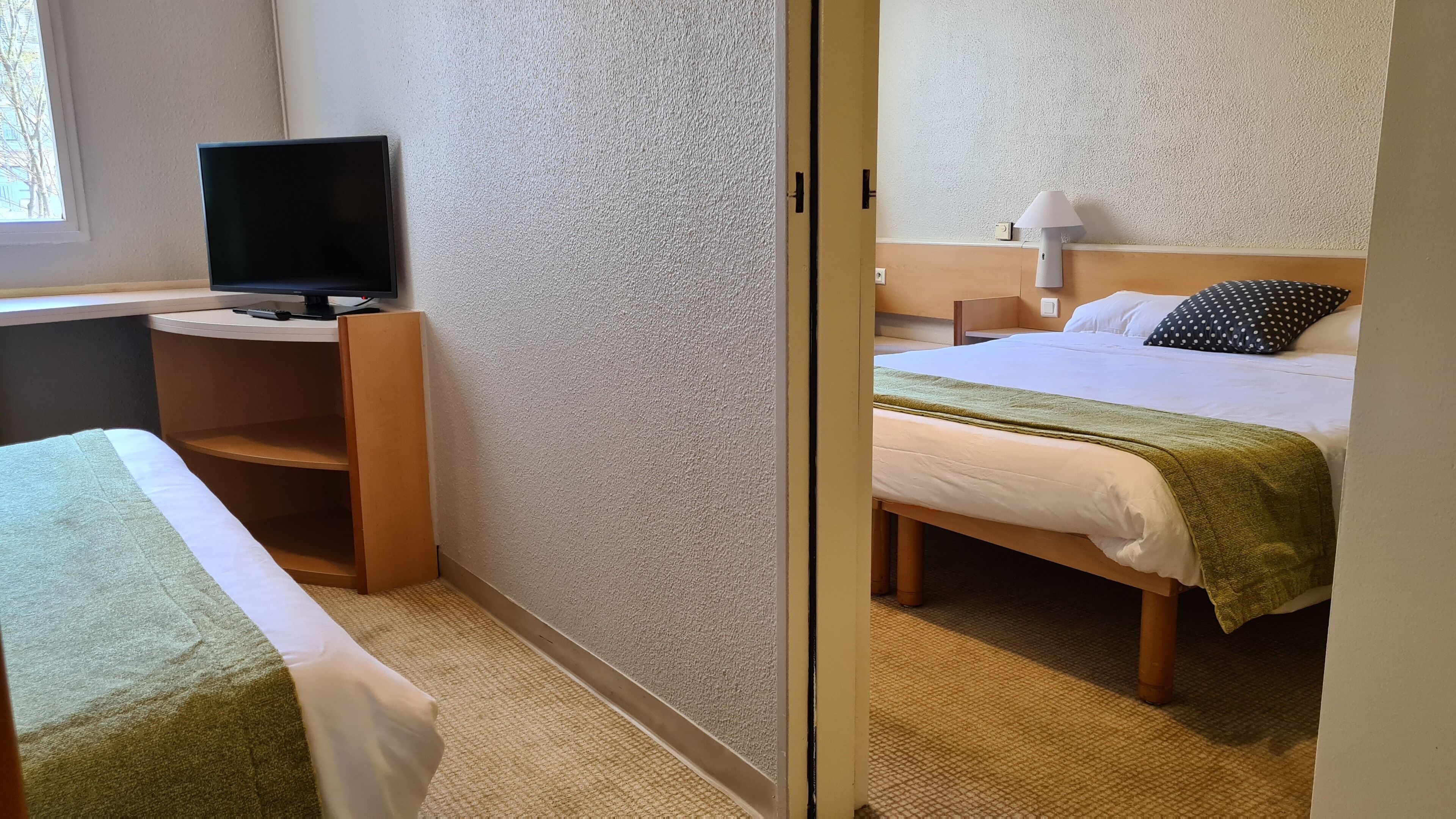A hotel room with a bed, a desk with a computer, and a window.