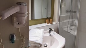 Un baño moderno con cabina de ducha de vidrio, un lavamanos blanco y un secador de pelo en un soporte de pared.