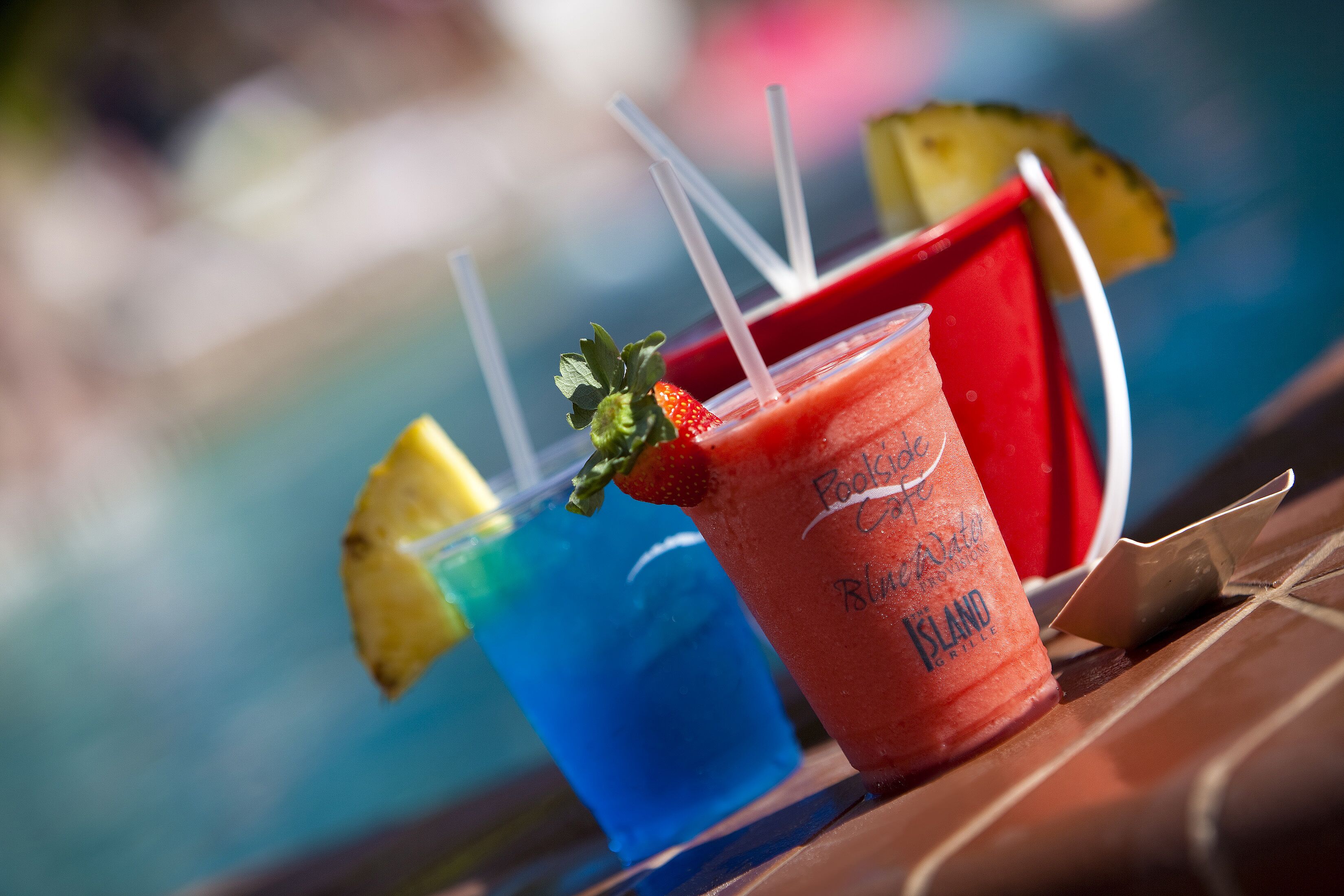 A poolside setting with a drink in a red cup labeled "Island Breeze" and a blue drink in the background.