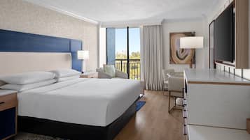 A hotel room with a large bed, a desk, a TV, and a balcony with a view.