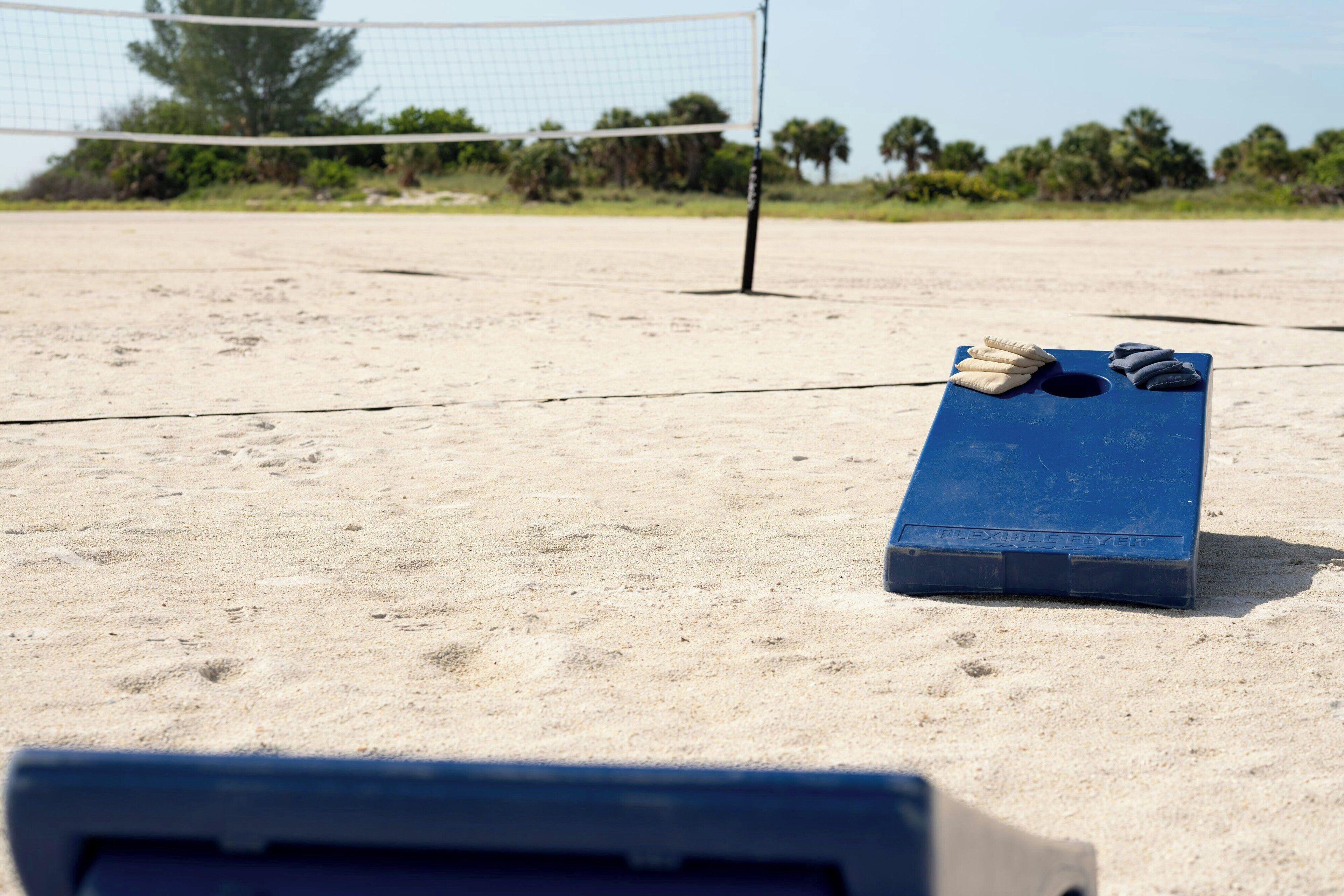 Un terrain de beach-volley avec un filet bleu, une planche bleue où sont posées des serviettes, et une surface sablonneuse.
