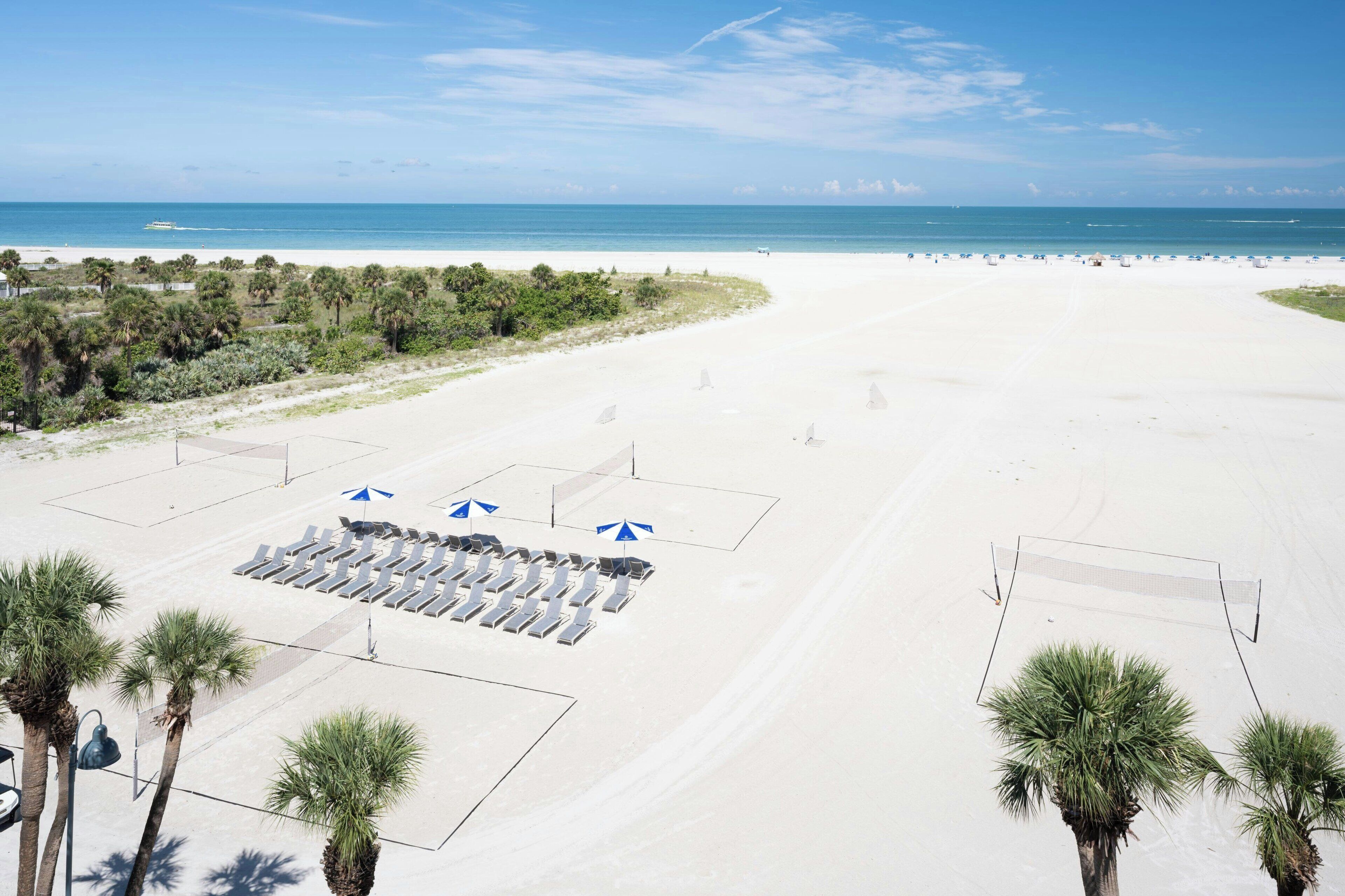 A beach with rows of sun loungers and umbrellas, palm trees, and a clear view of the ocean.