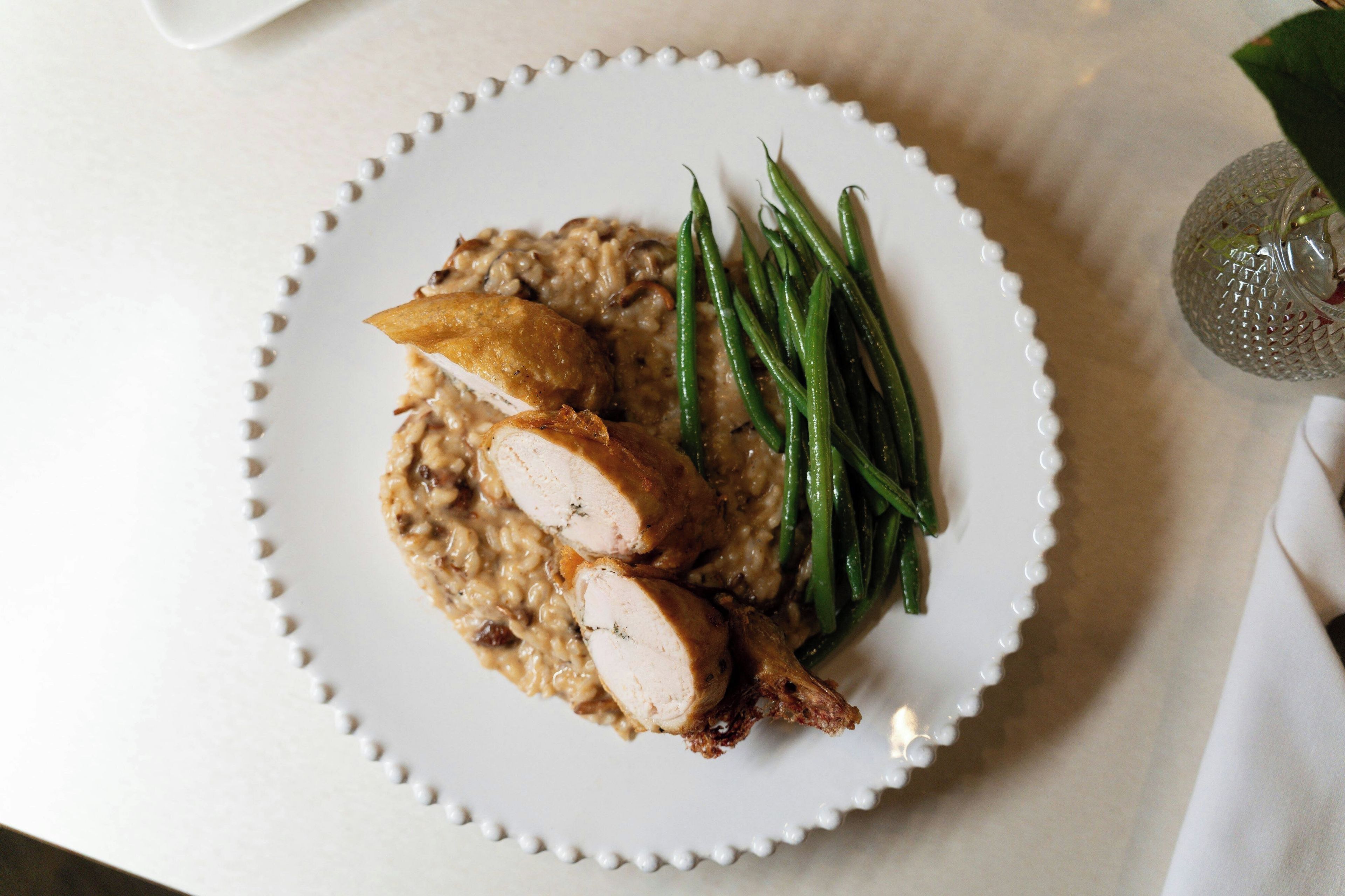 A plate with sliced meat, rice, and green beans on a white plate with a decorative edge.
