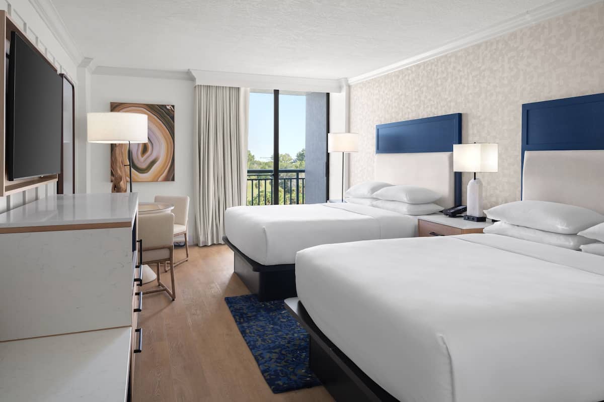 A hotel room with two beds, a desk, and a TV.