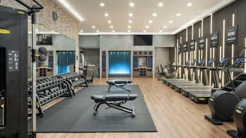 A gym with weight machines, dumbbells, treadmills, and a mirrored wall.