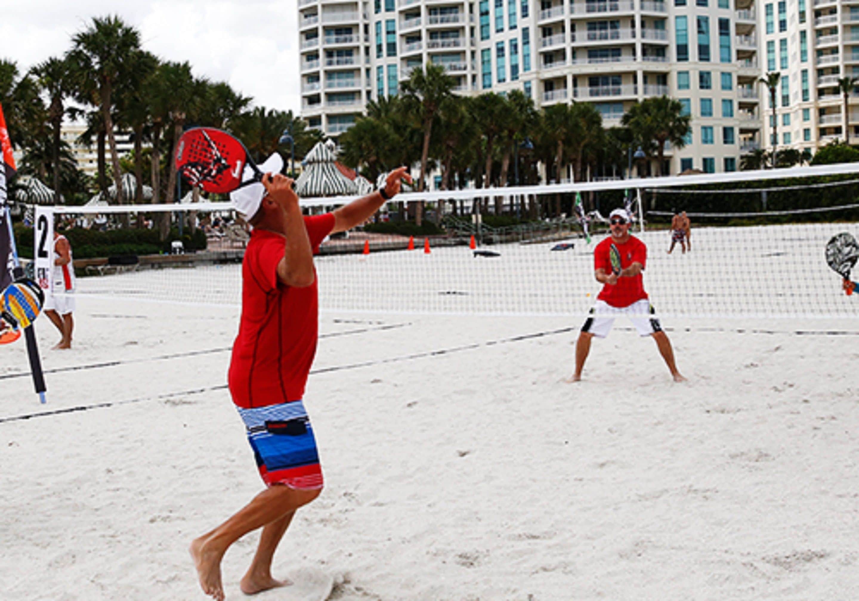 A beach volleyball game with players in red and white uniforms.