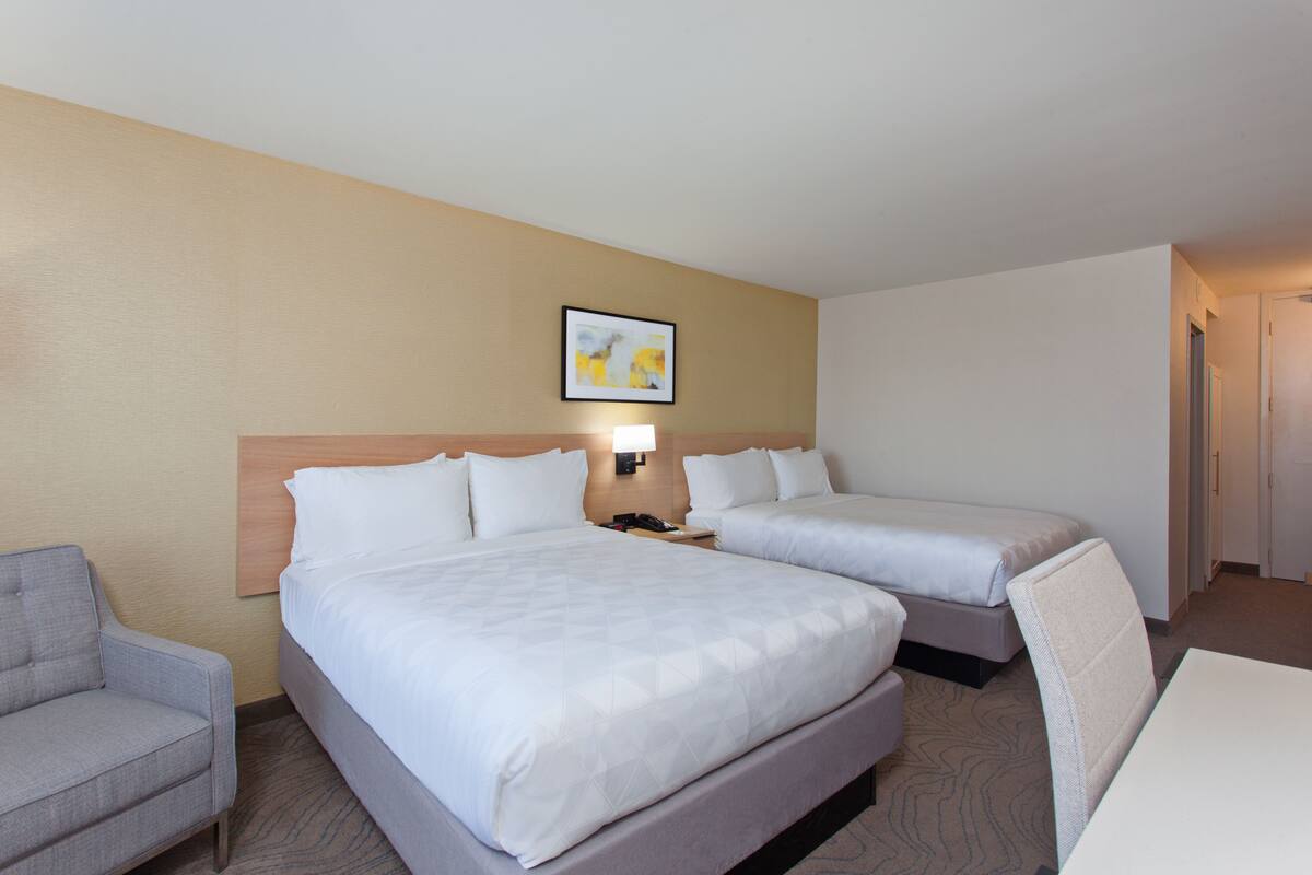A hotel room with two beds, a desk, a chair, and a sofa.