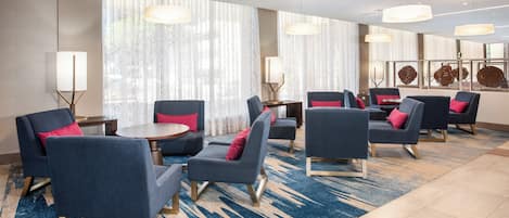 A hotel lobby with multiple seating areas, including sofas and armchairs, arranged around a central coffee table.
