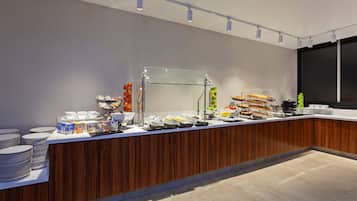 A buffet setup with various food items and beverages, including a glass display case and a coffee station.