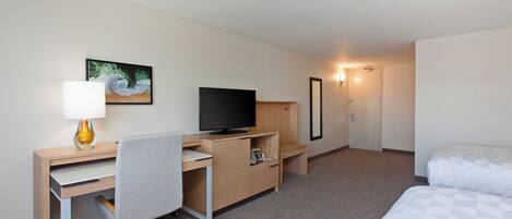 A hotel room with a desk, chair, television, bed, and a painting on the wall.