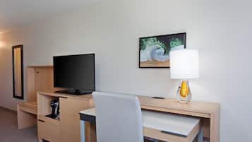 Habitación de hotel con una televisión de pantalla plana, un escritorio con lámpara, una silla y un cuadro en la pared.