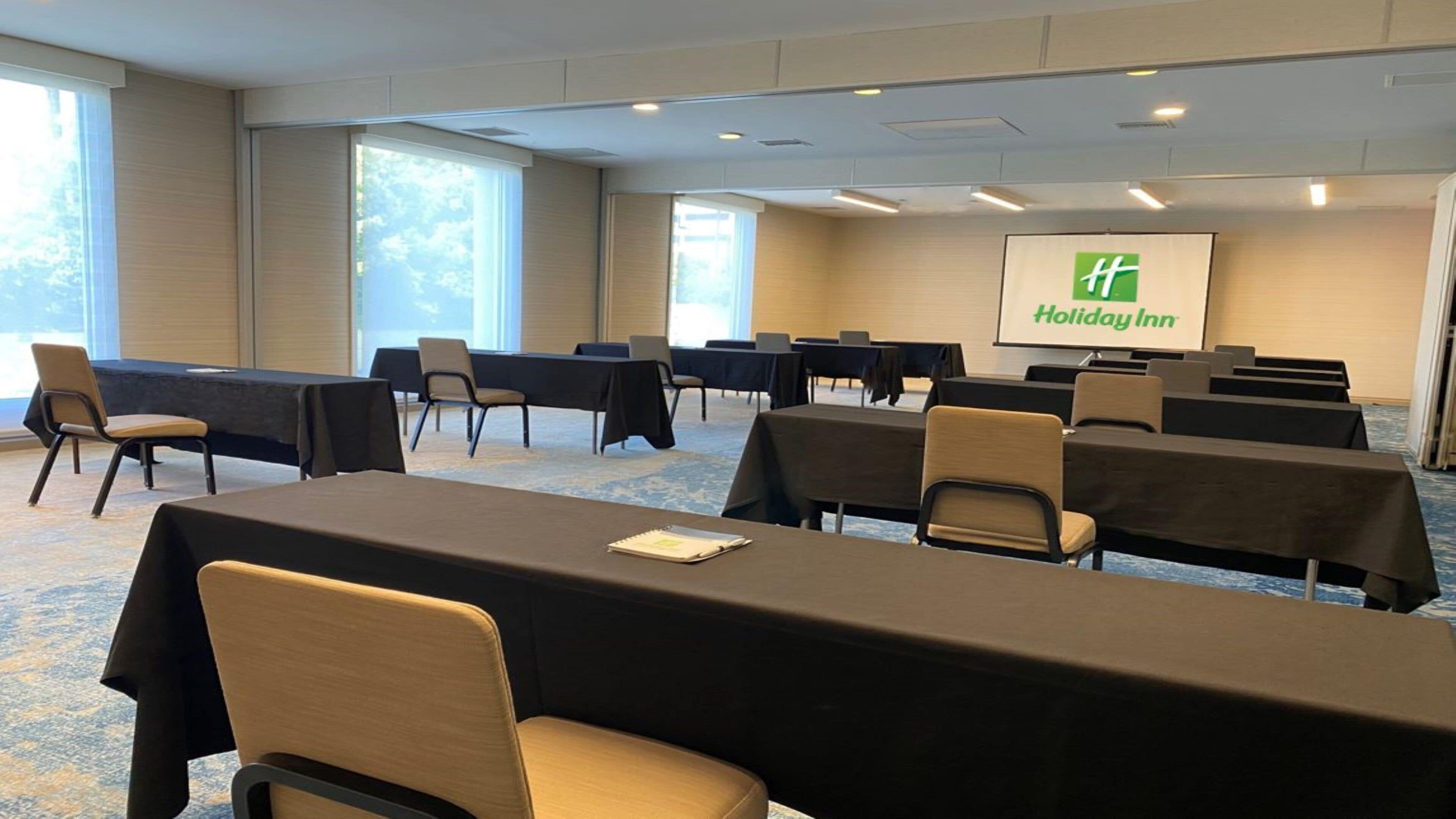 Un salón de conferencias con mesas, sillas y una pantalla de proyector mostrando el logotipo de Holiday Inn.