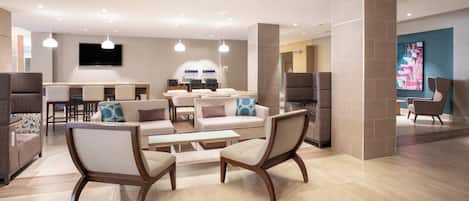 Un hall d’hôtel moderne, doté d’espaces aménagés avec des sièges, d’un téléviseur et d’un comptoir de réception.