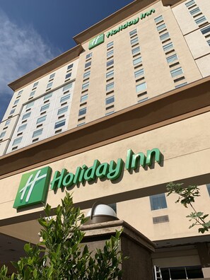 Ein Holiday Inn Hotelgebäude mit beiger Fassade, zahlreichen Fenstern und einem auffälligen grünen Logo.