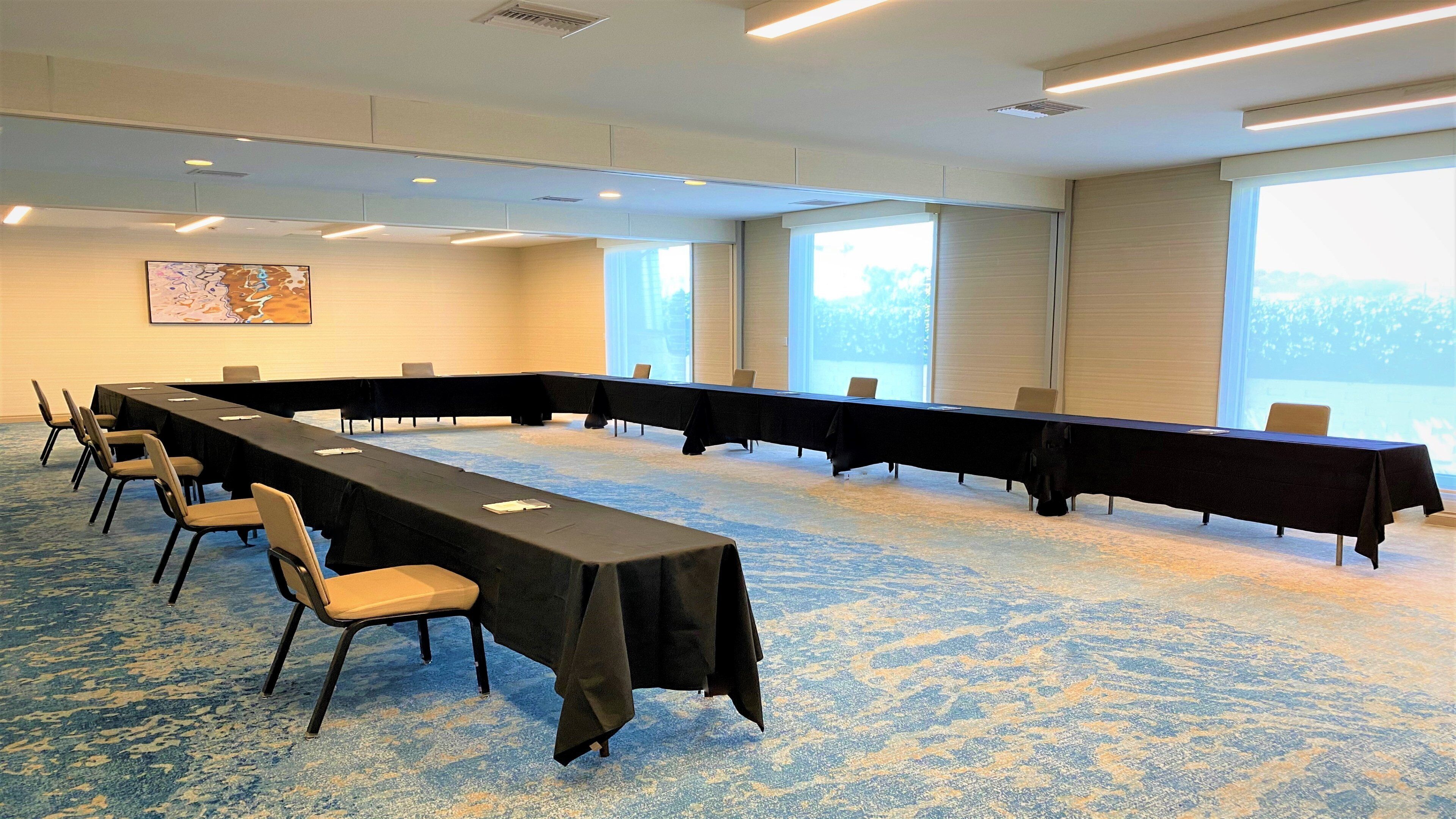Un salón de conferencias con una larga mesa, sillas y ventanas amplias.
