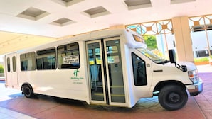 Un autobus de navette blanche de la chaîne Holiday Inn, desservant l’aéroport LAX, est garé devant l’entrée d’un terminal.