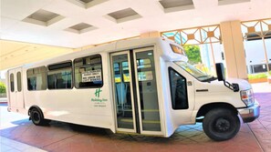 Ein weißer Shuttlebus des Holiday Inn LAX Airport parkt vor einem Terminaleingang.