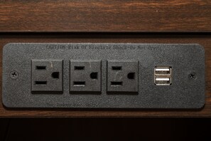 A black electrical outlet with three sockets and a USB port on a wooden surface. - Red Roof Inn Knoxville Central - Papermill Road (Knoxville)