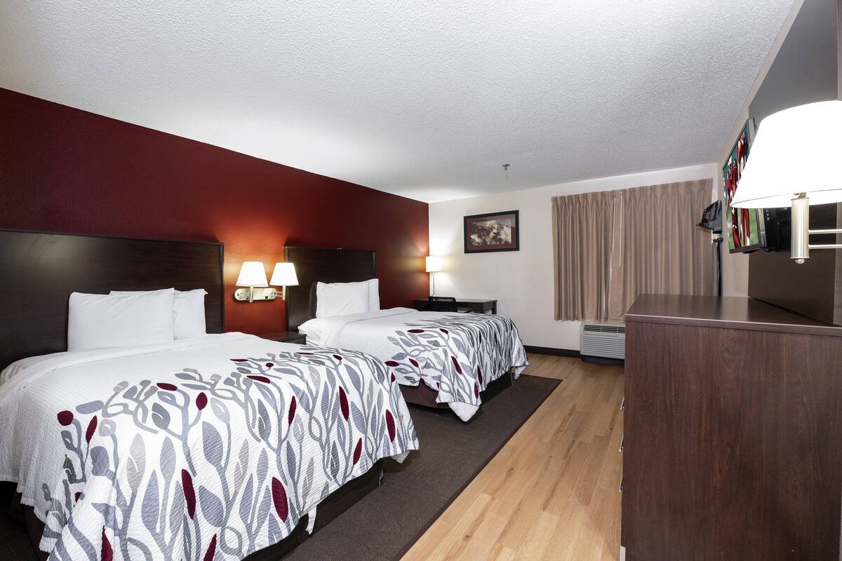 A hotel room with two beds, a desk, a TV, and a lamp.