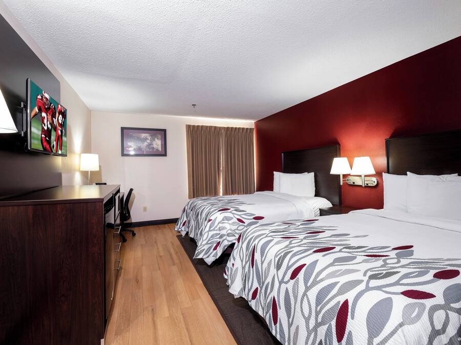 Quarto de hotel com escrivaninha, duas camas, televisão e janela com cortinas.
