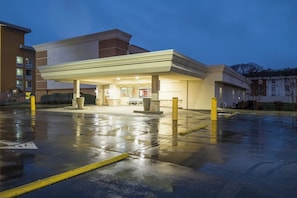 A hotel with a gas station attached, featuring a wet parking lot and a well-lit entrance.