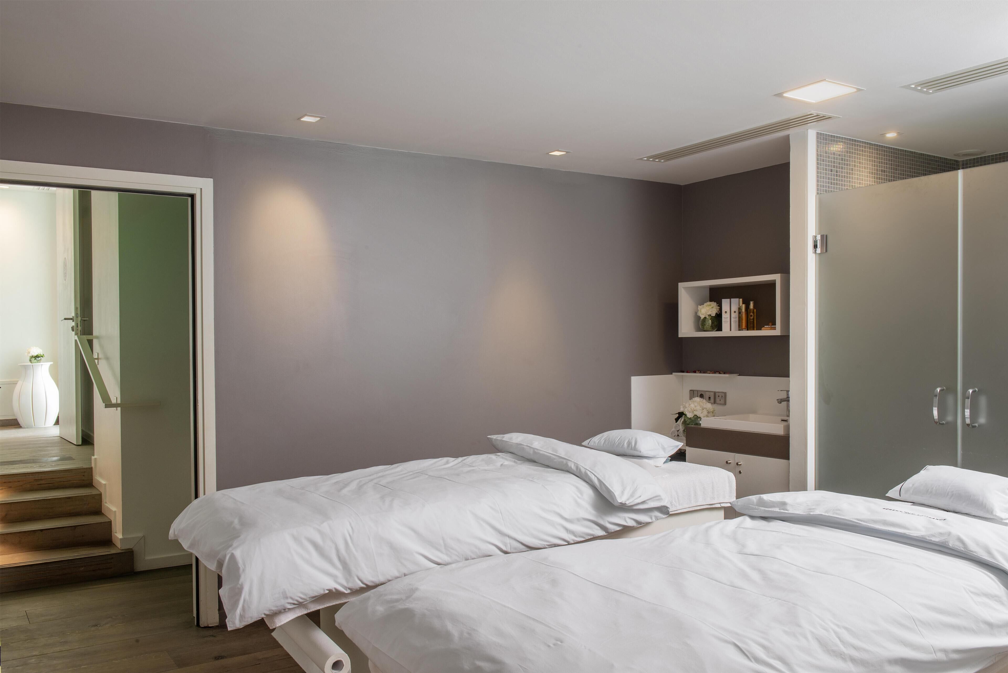 A modern bedroom with two beds, a walk-in closet, and a bathroom with a vanity.