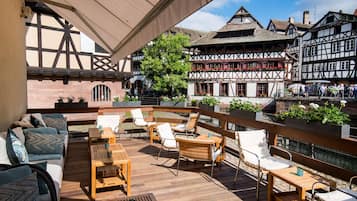 Een terras met houten meubels en uitzicht op historische vakwerkhuizen.