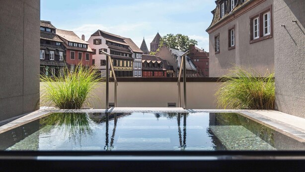 Une piscine intérieure moderne offrant une vue dégagée sur l’architecture européenne traditionnelle en arrière-plan.