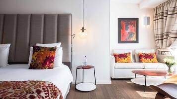 A modern hotel room with a large bed, a sofa, a small table, and a hanging light fixture.