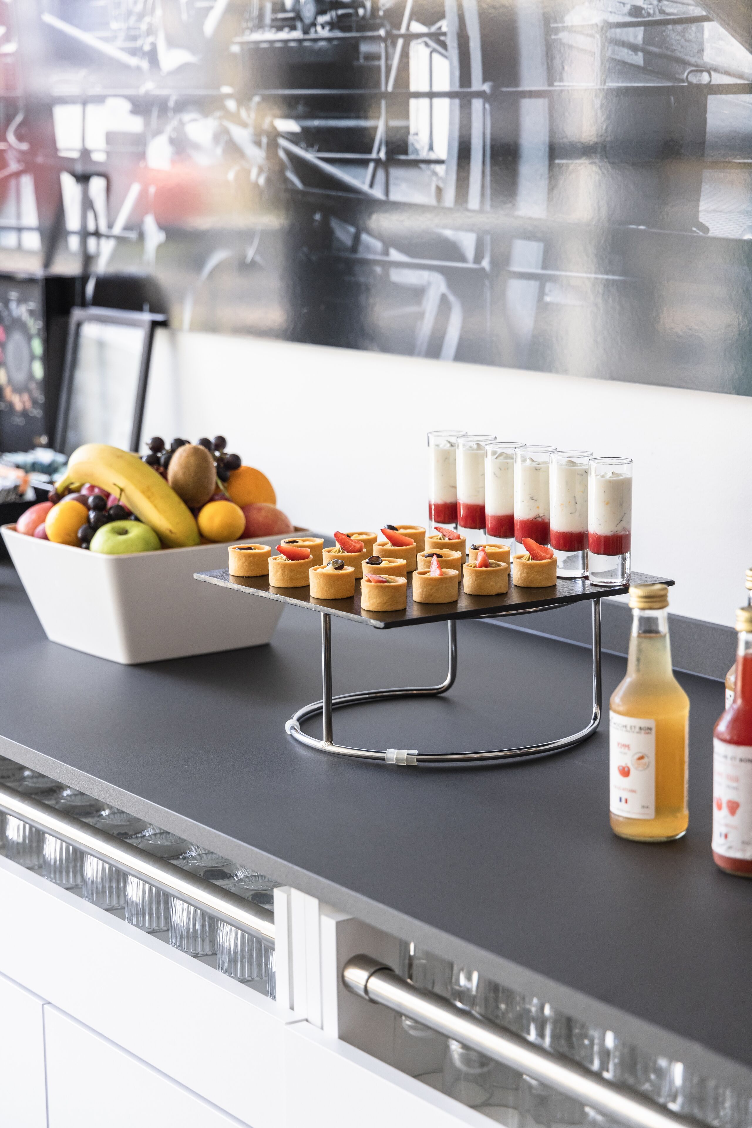 Un comptoir de cuisine avec un panier de fruits, des mini-desserts et des bouteilles de boissons.