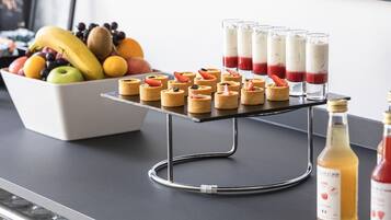 Un comptoir de cuisine avec un panier de fruits, des mini-desserts et des bouteilles de boissons.