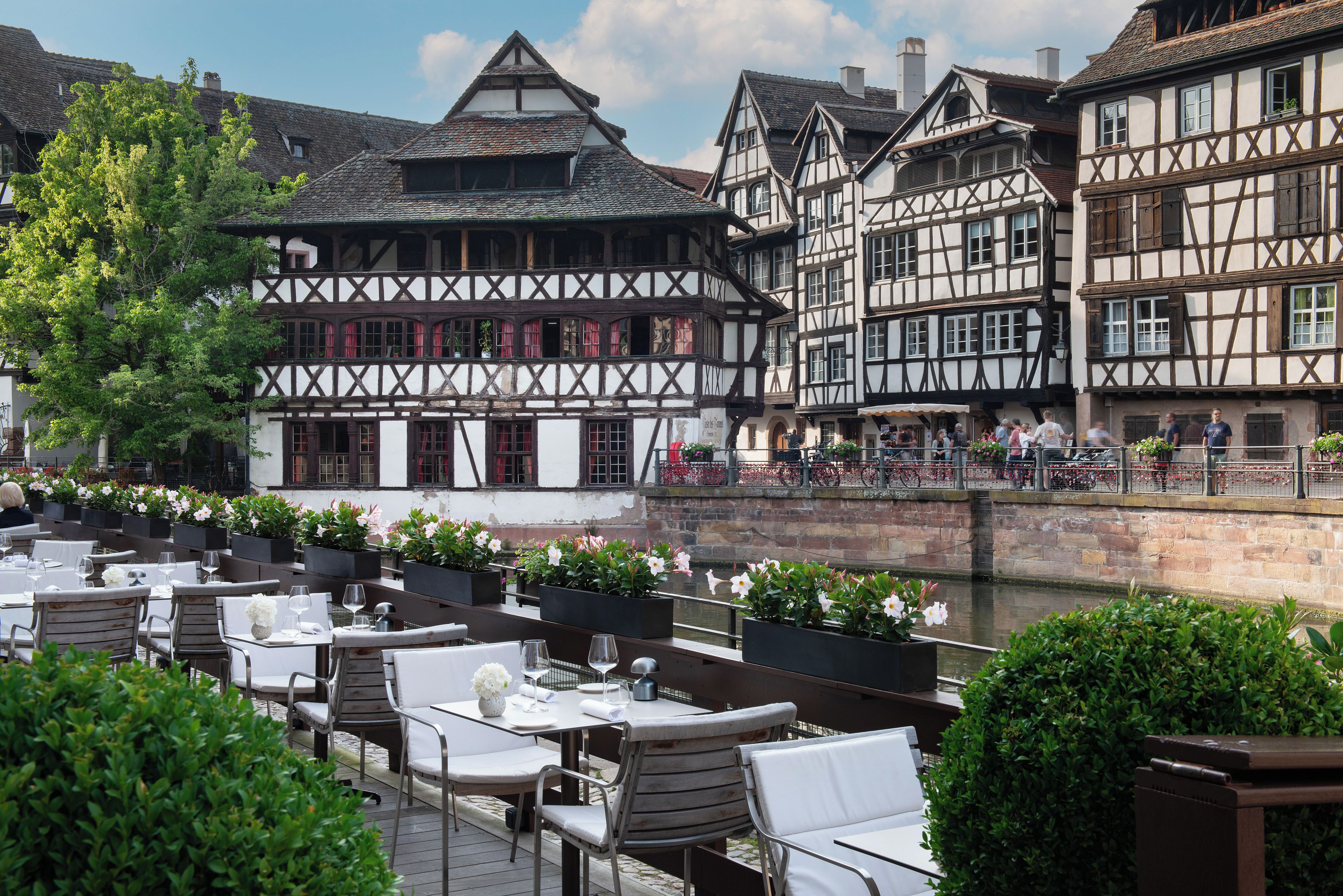 A riverside café with outdoor seating overlooking a historic building with timber framing.