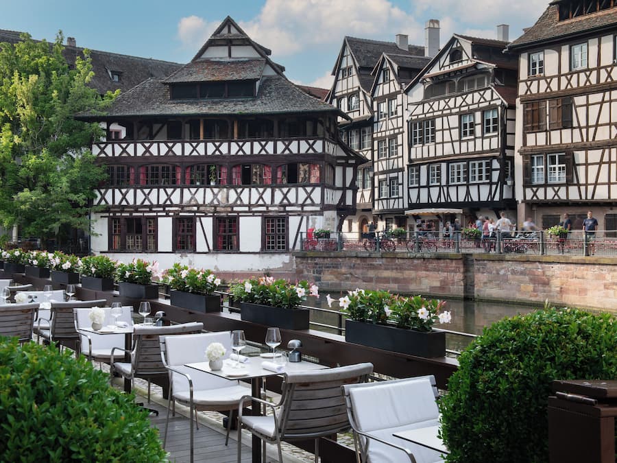 Een café aan de rivier met terras, met uitzicht op een historisch pand met vakwerkkonstructie.