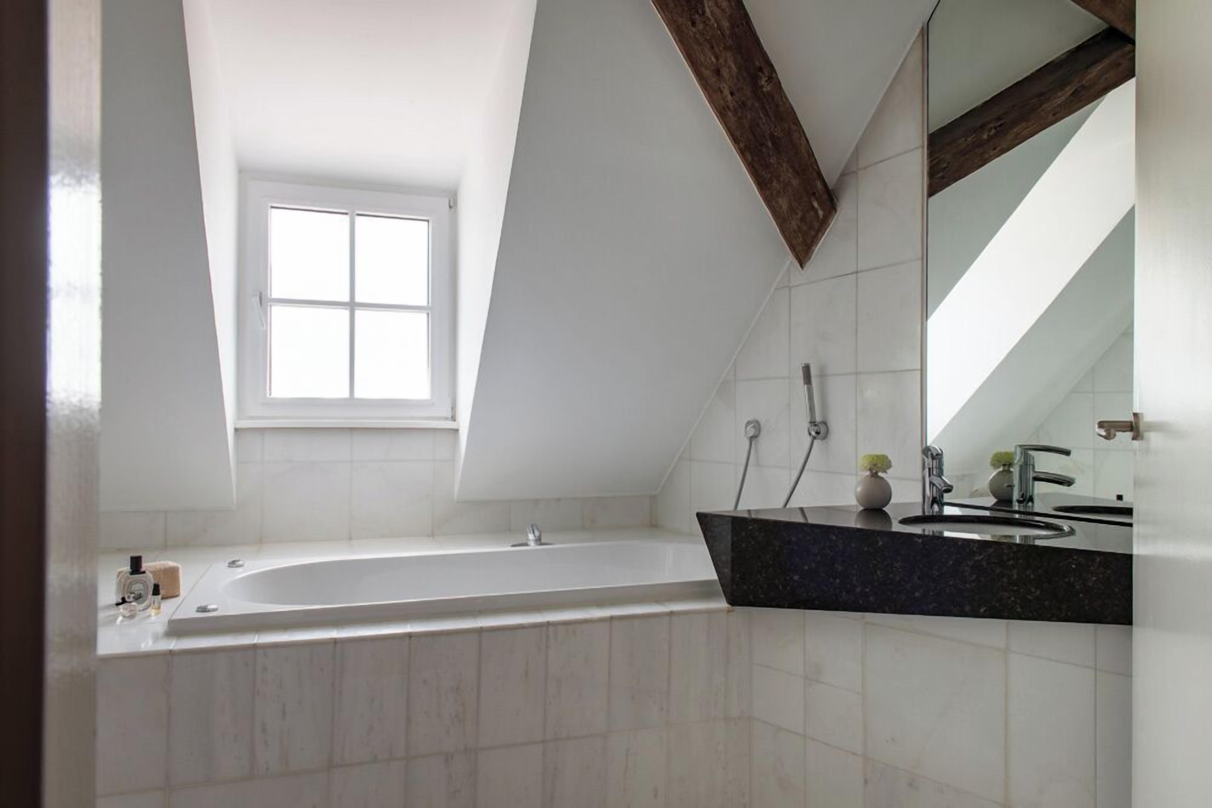 A modern bathroom with a freestanding bathtub, a large mirror, and a window providing natural light.