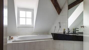 Une salle de bain moderne avec une baignoire sur pieds, un grand miroir et une fenêtre laissant entrer la lumière naturelle.
