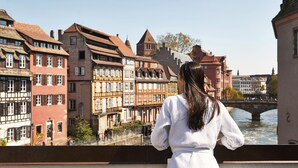 Une femme se tient sur un pont surplombant une rivière, avec des bâtiments historiques en arrière-plan.