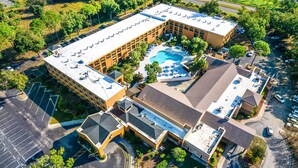 An aerial view of a hotel with a swimming pool, multiple parking lots, and surrounding greenery. - Mi Casa Hotel (Orlando)