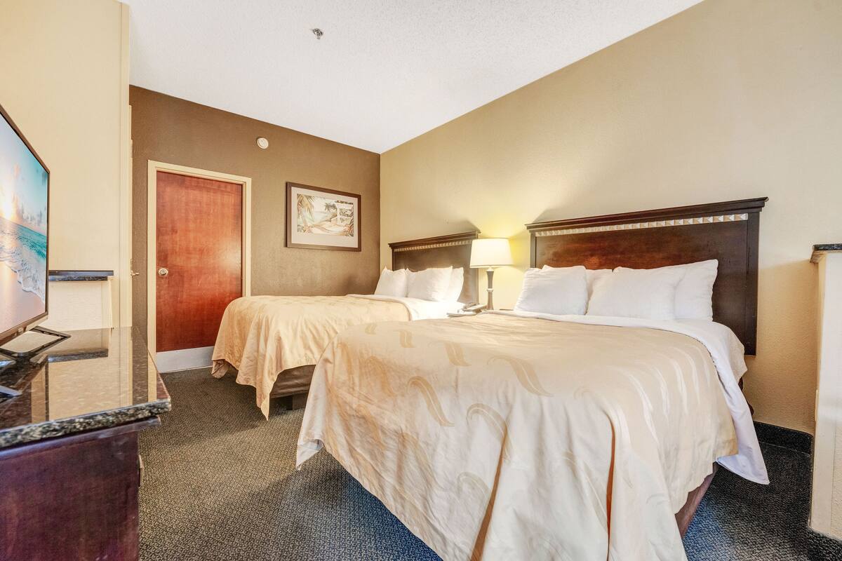 A hotel room with two beds, a desk, a door, and a wall-mounted picture.