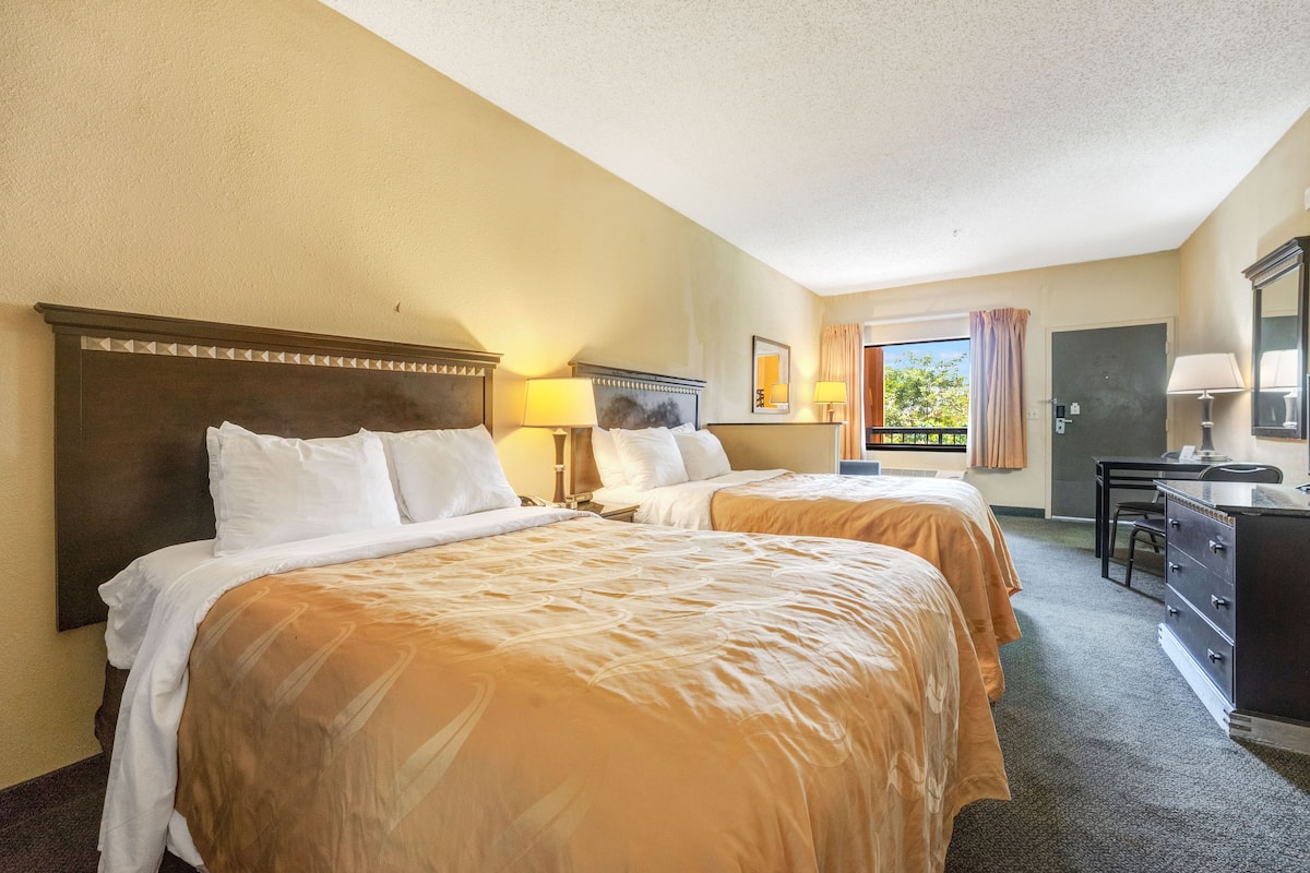 A hotel room with two beds, a desk, and a chair.