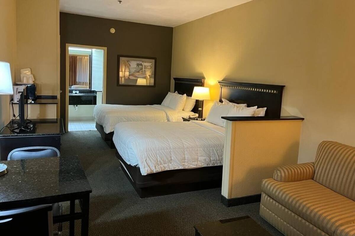 A hotel room with two beds, a desk, a chair, a sofa, and a painting on the wall.