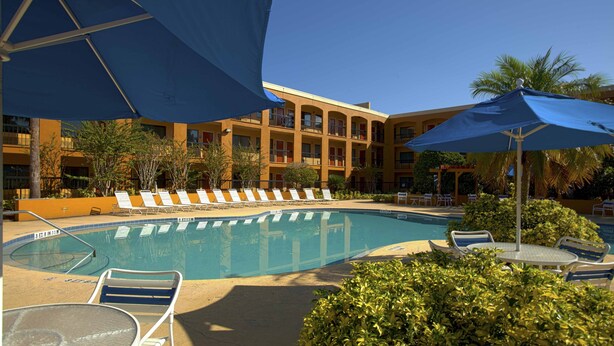 A pool area with lounge chairs and umbrellas, surrounded by a building with balconies. - Mi Casa Hotel (Orlando)