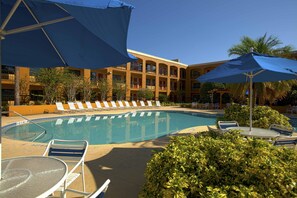 A pool area with lounge chairs and umbrellas, surrounded by a building with balconies. - Closed - Mi Casa Hotel (Orlando)