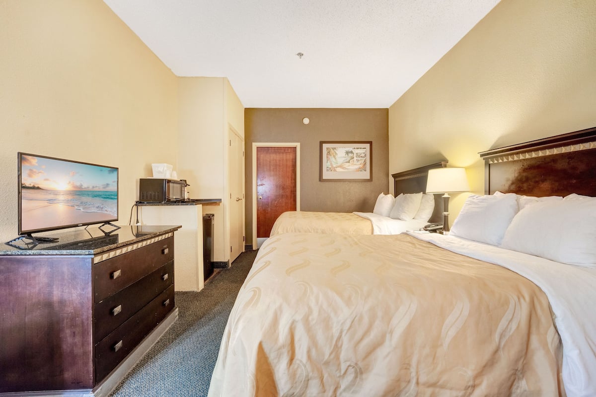 A hotel room with a bed, a desk with a television, a microwave, and a door leading to another room.