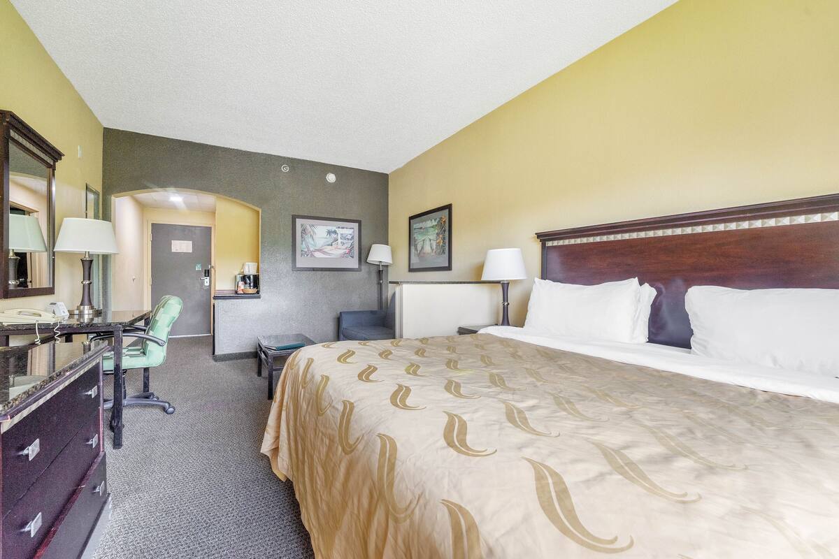 A hotel room with a bed, desk, chair, dresser, and a bathroom door.