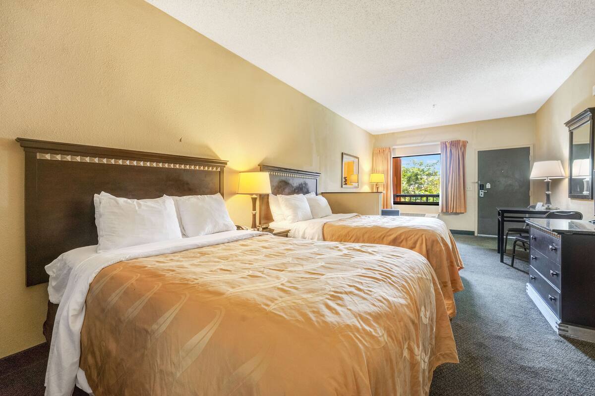 A hotel room with two beds, a desk, a chair, and a window with a view.