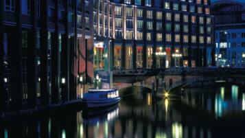 Un hôtel à plusieurs étages, doté d’une façade moderne, situé au bord d’un canal où naviguent des bateaux.