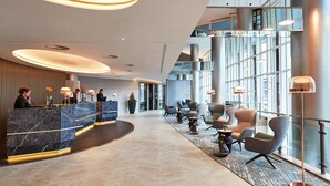 A modern hotel lobby with a reception desk, seating area, and large windows. - Steigenberger Hotel Hamburg (Hamburg)